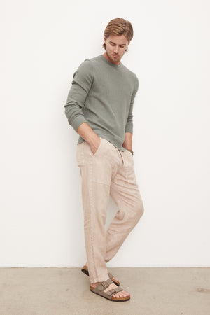 A man wearing tan linen pants and a green long-sleeve Velvet by Graham & Spencer ACE THERMAL CREW.