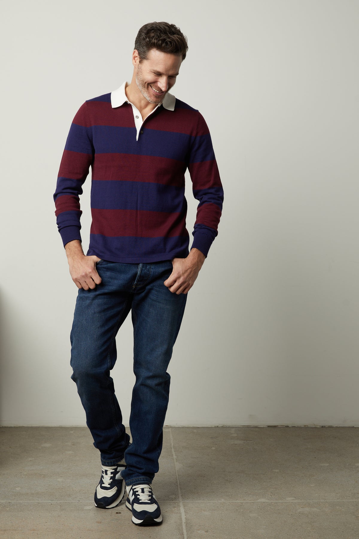 A man in a Velvet by Graham & Spencer Hastings Striped Polo Sweater is standing in front of a wall.-35678517297345
