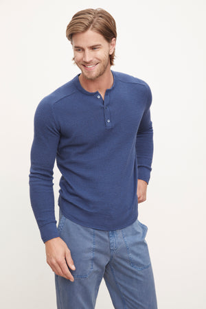 A man wearing a Velvet by Graham & Spencer JAKE THERMAL HENLEY sweater and blue pants.