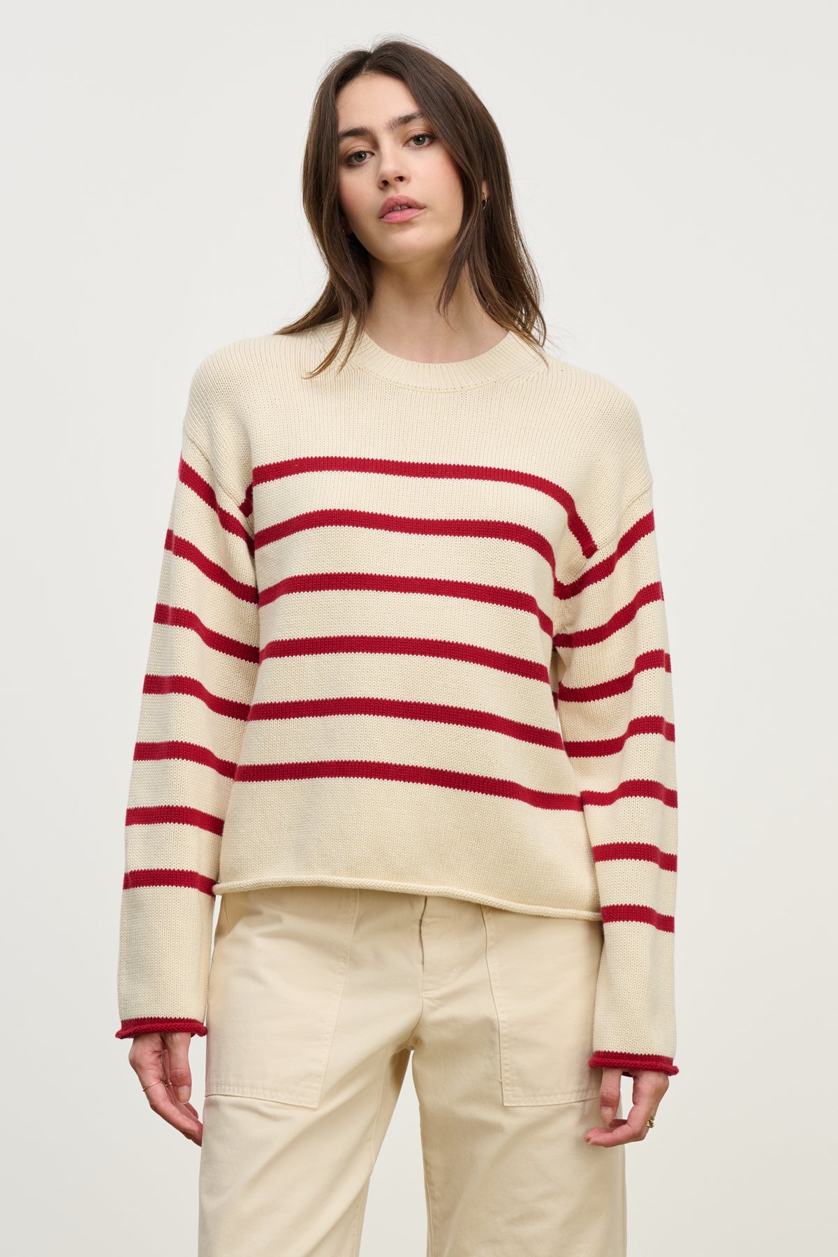 A woman wears the LUCIA SWEATER by Velvet by Graham & Spencer, a relaxed-fit cotton-cashmere crewneck with red stripes, paired with beige pants against a plain light background.
