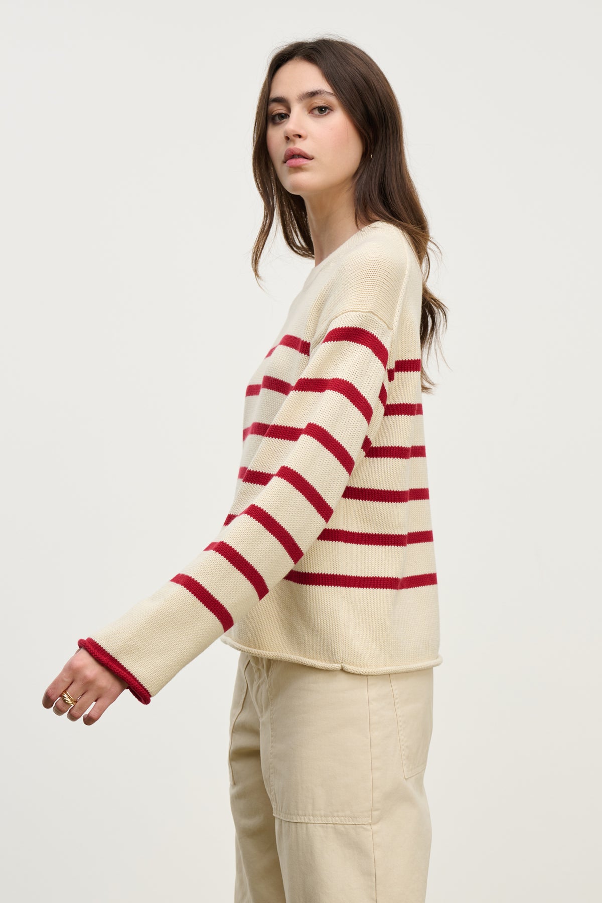 A woman wears the LUCIA SWEATER by Velvet by Graham & Spencer, a relaxed-fit cotton-cashmere piece with red stripes, paired with beige pants against a plain light background.