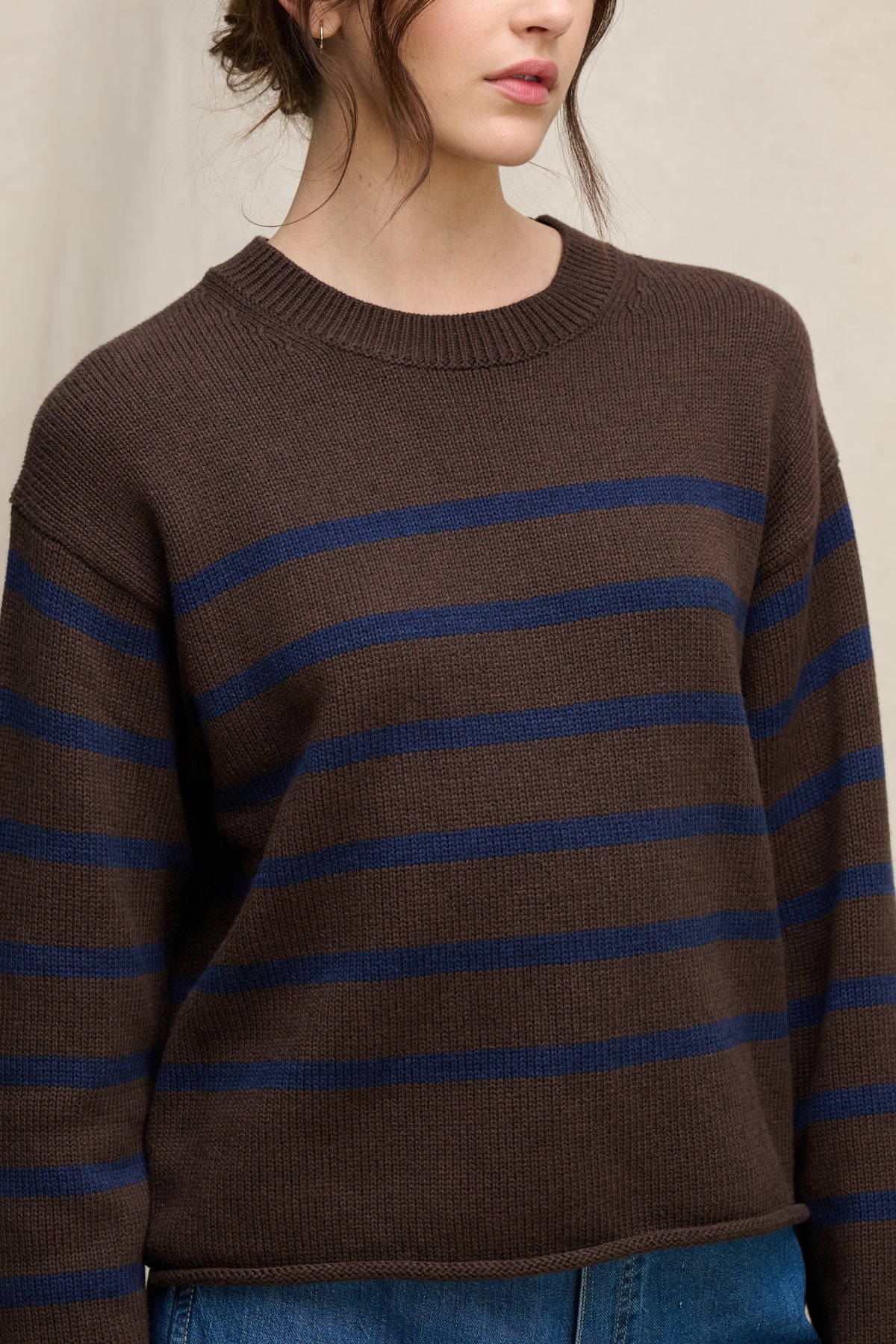   A person wearing the LUCIA COTTON CASHMERE SWEATER by Velvet by Graham & Spencer—a relaxed-fit brown crewneck with horizontal navy stripes—paired with blue jeans, shown from shoulders to waist. 