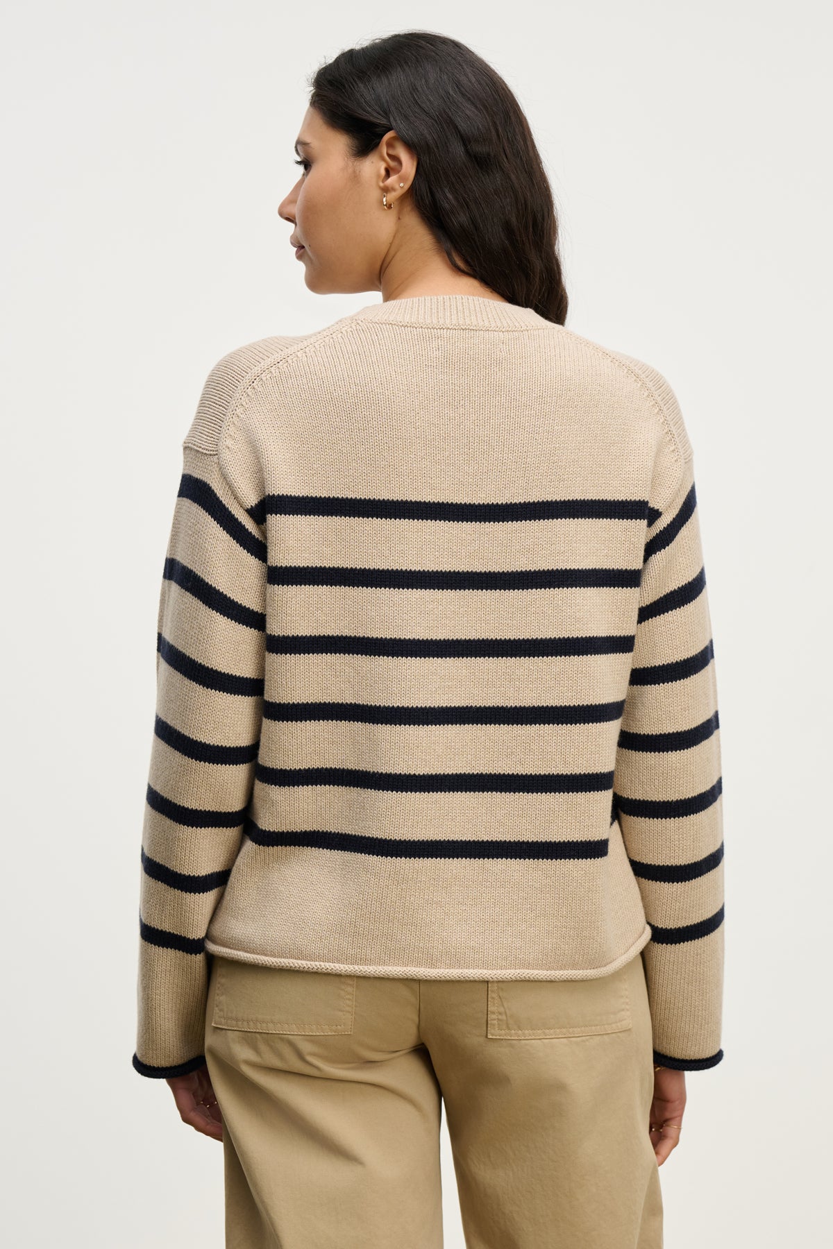 A person with long dark hair, seen from behind, wears the LUCIA SWEATER by Velvet by Graham & Spencer—a relaxed-fit, cotton-cashmere striped crewneck—paired with beige pants against a plain background.-40227097772225