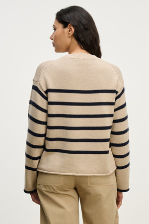 A person with long dark hair, seen from behind, wears the LUCIA SWEATER by Velvet by Graham & Spencer—a relaxed-fit, cotton-cashmere striped crewneck—paired with beige pants against a plain background.