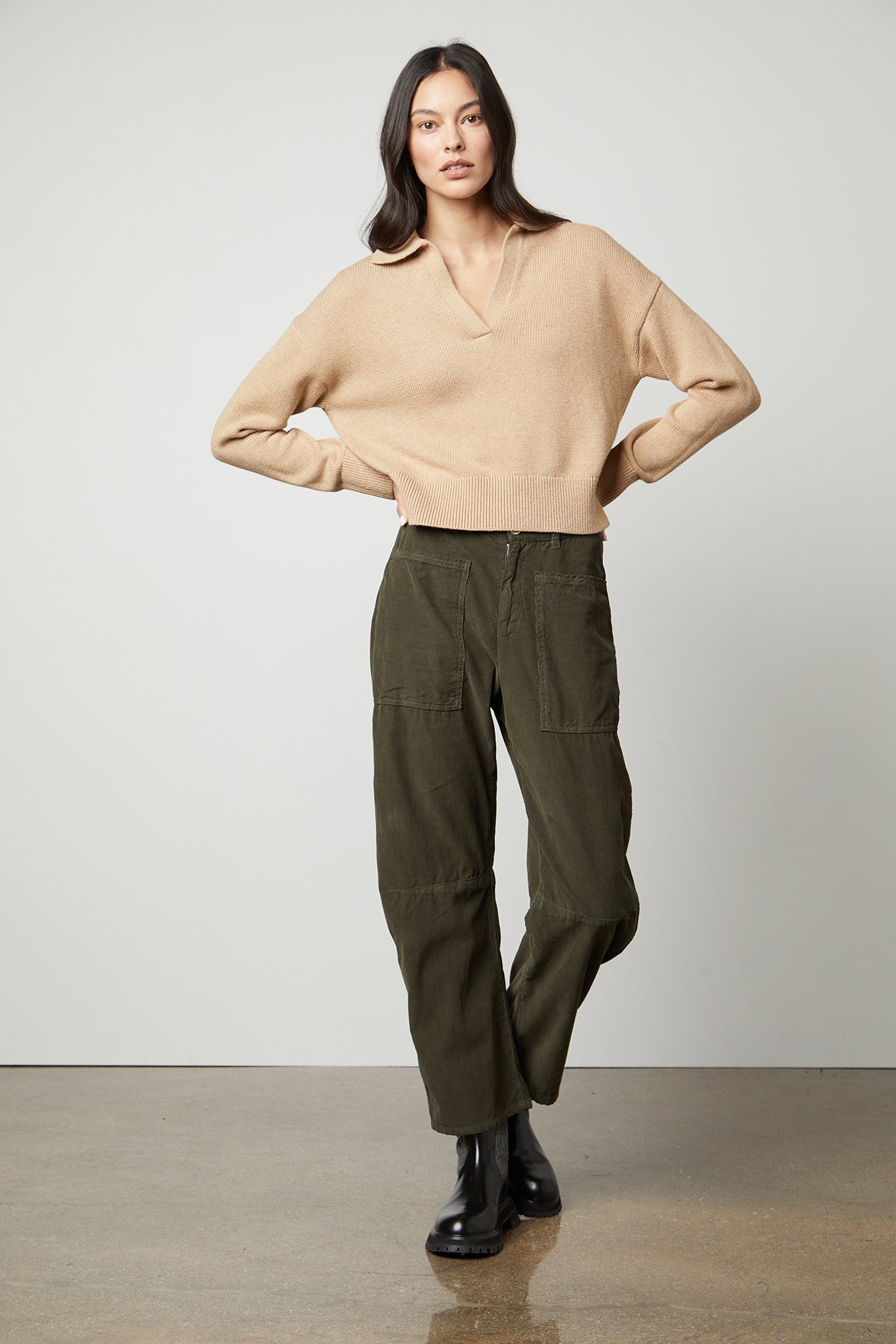 The model is wearing a Velvet by Graham & Spencer LUCIE POLO SWEATER with a ribbed V-neckline and olive cargo pants.-35503528181953