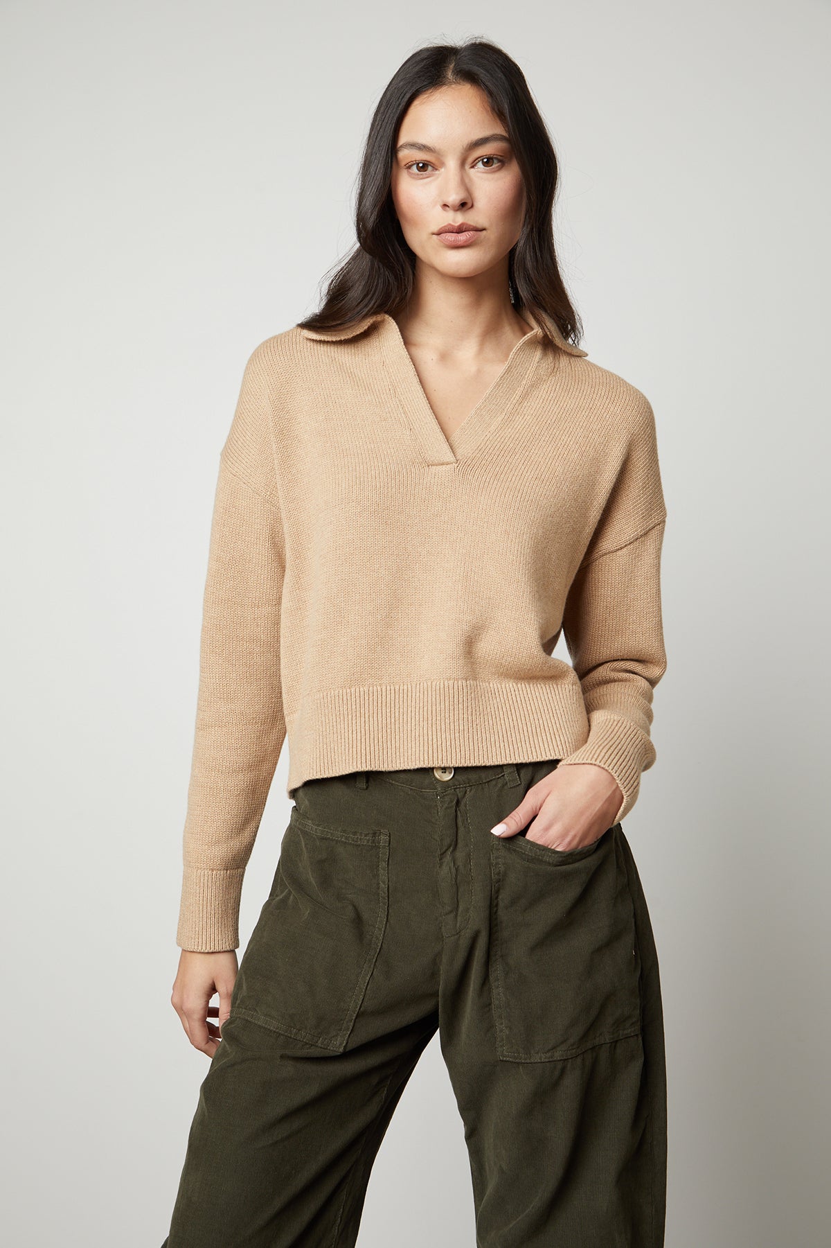 The model is wearing a layered LUCIE POLO SWEATER by Velvet by Graham & Spencer with a ribbed V-neckline, paired with olive pants.-35503525986497
