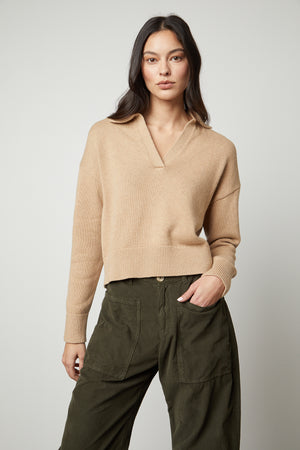 The model is wearing a layered LUCIE POLO SWEATER by Velvet by Graham & Spencer with a ribbed V-neckline, paired with olive pants.