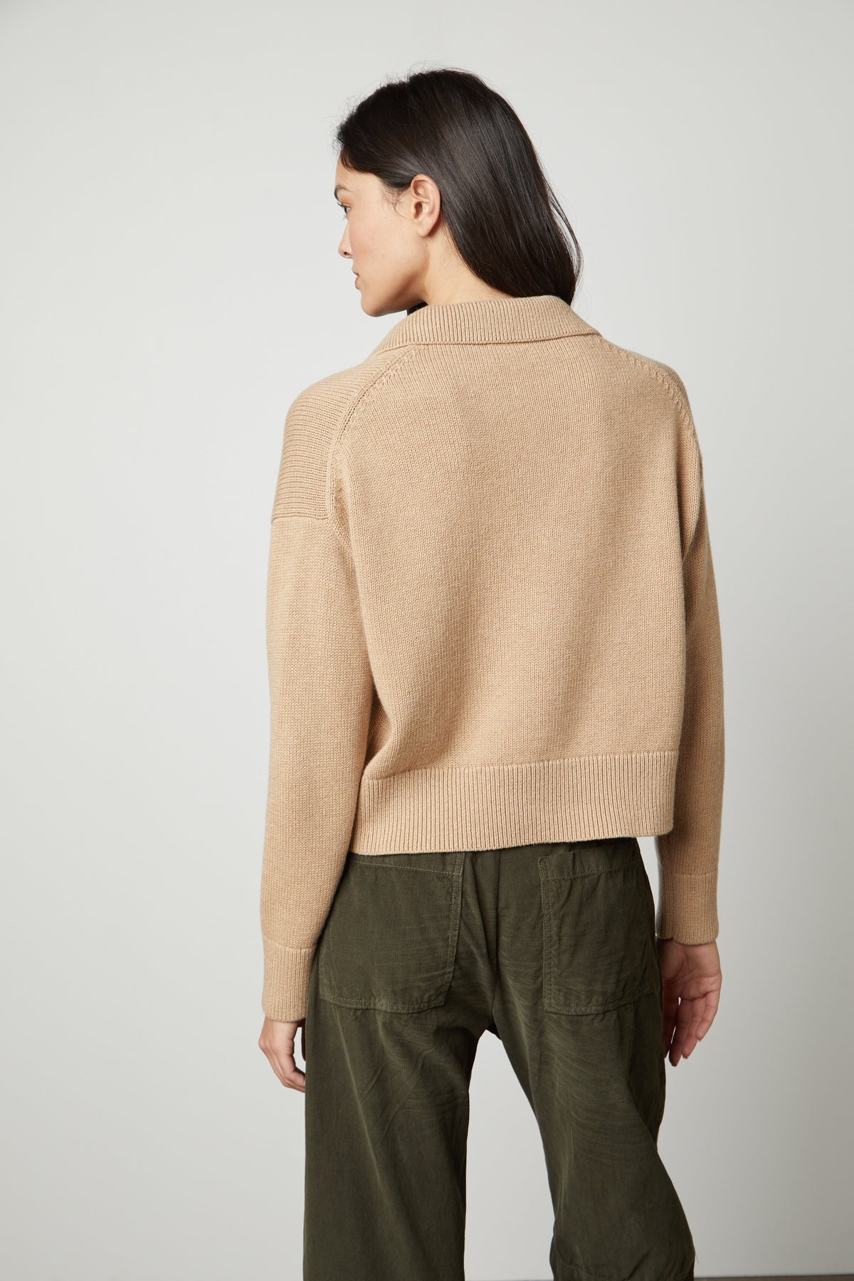 The back view of a woman wearing a Velvet by Graham & Spencer LUCIE POLO SWEATER with a ribbed V-neckline, paired with olive pants.-35446429614273