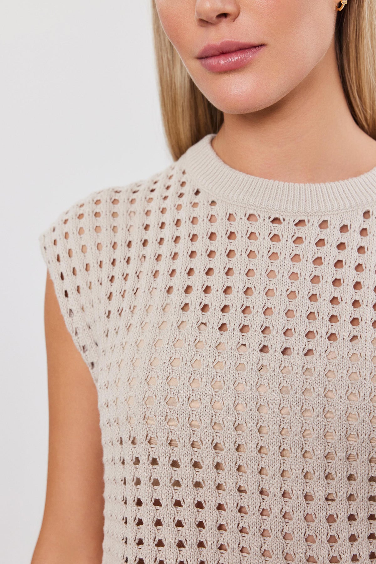   Close-up of a woman wearing a beige cotton cashmere sleeveless MAISON SWEATER, focusing on the intricate pattern of the knitwear by Velvet by Graham & Spencer. 