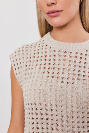 Close-up of a woman wearing a beige cotton cashmere sleeveless MAISON SWEATER, focusing on the intricate pattern of the knitwear by Velvet by Graham & Spencer.