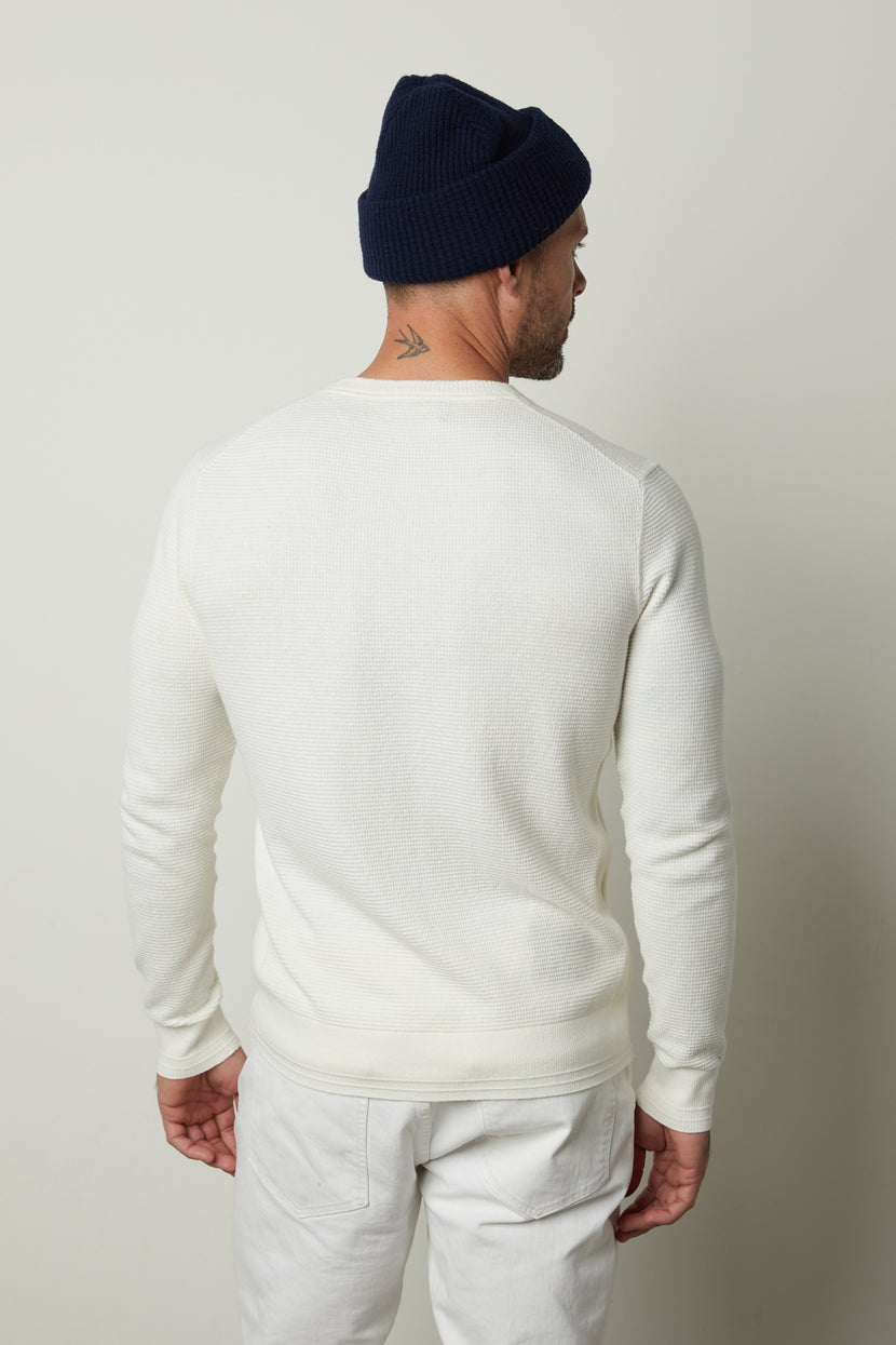 A person wearing the WALTER SWEATER by Velvet by Graham & Spencer, white pants, and a navy blue knit hat stands facing away from the camera.