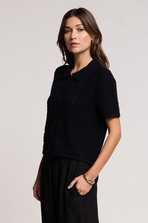A woman stands against a plain background, wearing the ROSEMOND CARDIGAN by Velvet by Graham & Spencer with black pants.