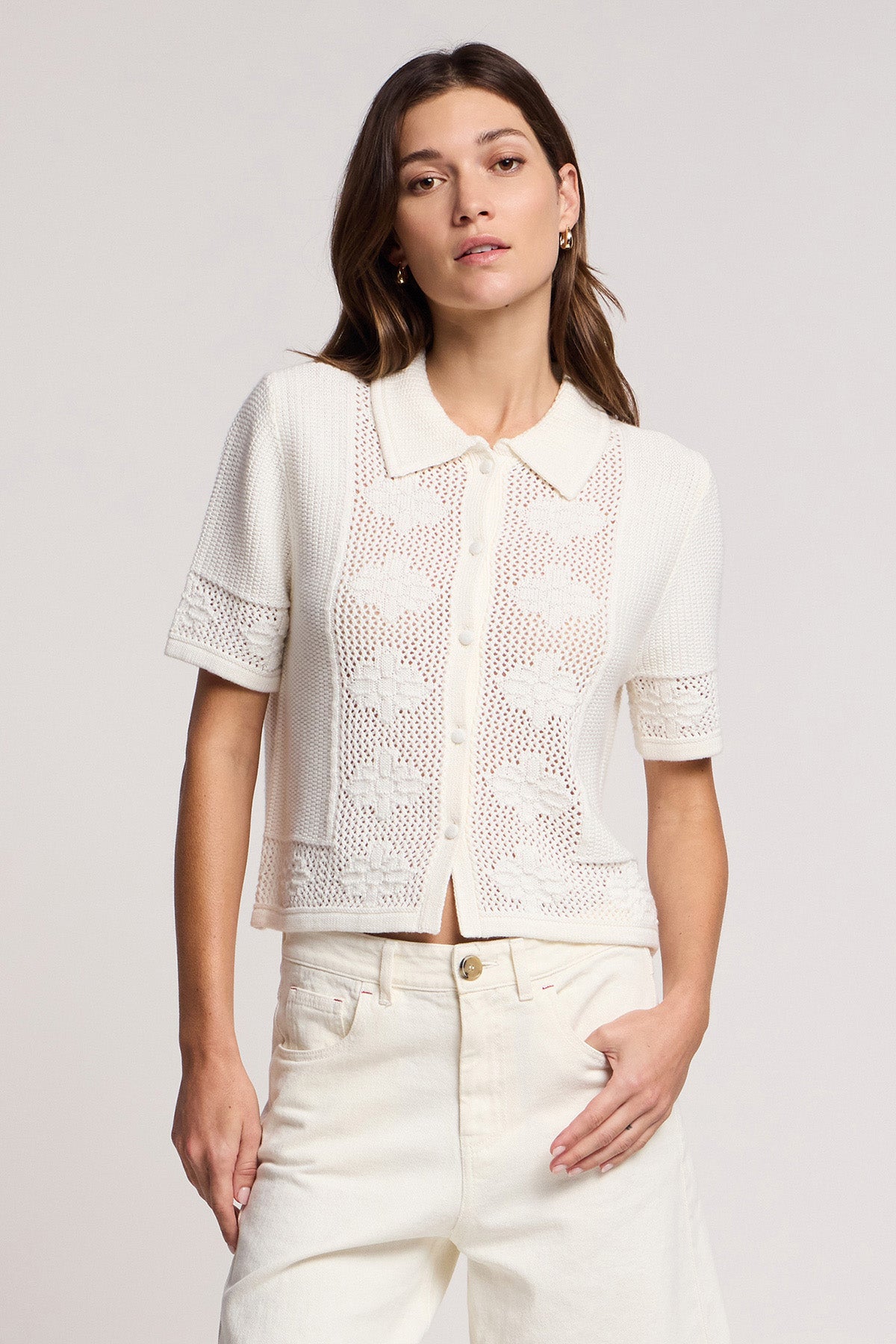 A woman wears the ROSEMOND CARDIGAN by Velvet by Graham & Spencer—a short-sleeve, button-up cream cotton-cashmere piece with mesh stitching and front pockets—paired with high-waisted cream pants, ideal as a transitional layer.-41372113010881