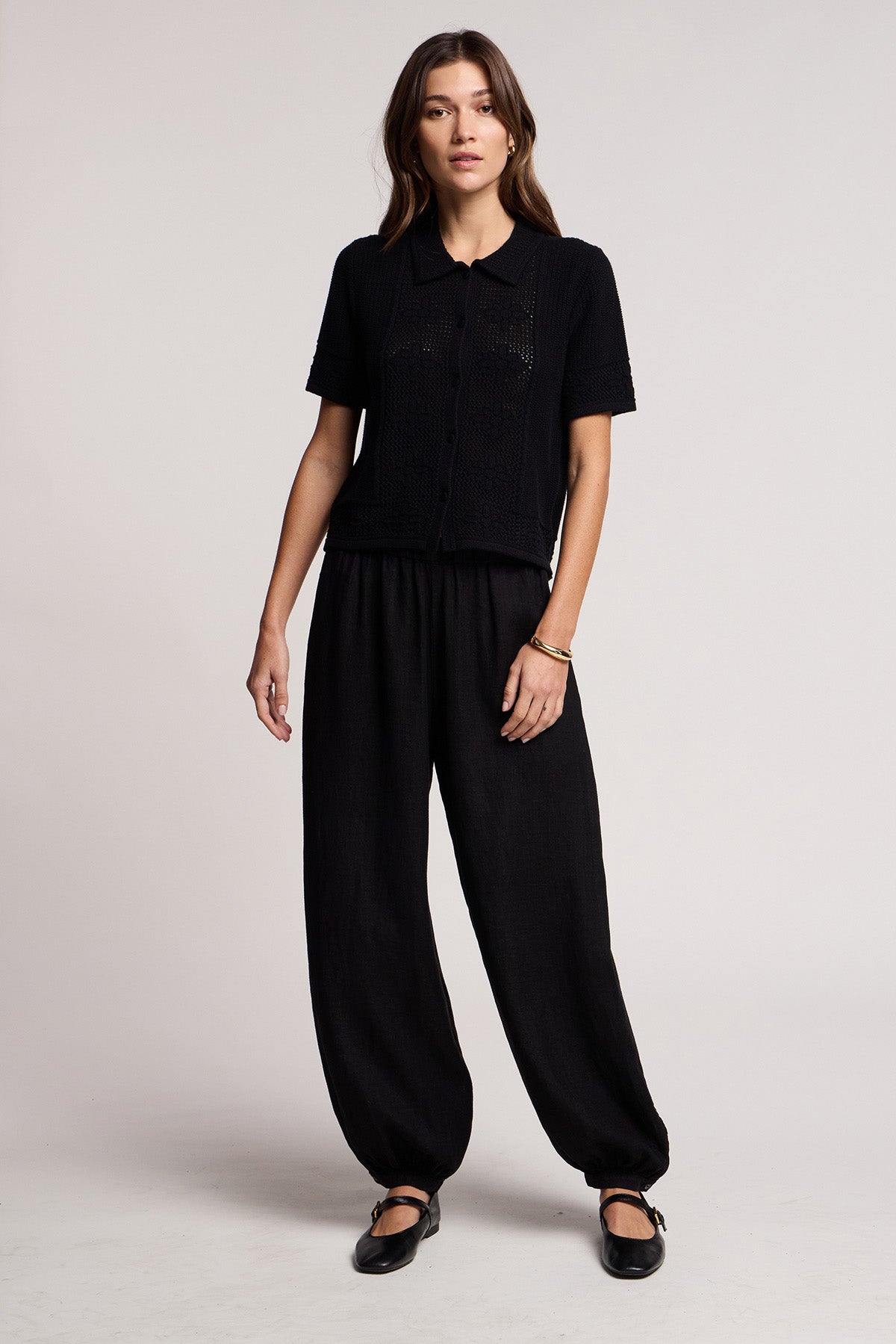 A woman stands facing forward against a plain light background, wearing black shoes, a black short-sleeve button-up shirt, and Velvet by Graham & Spencer's CAMBER LINEN PANT with an elastic waist.