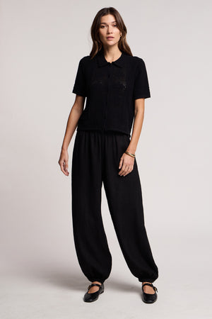 A woman stands facing forward against a plain light background, wearing black shoes, a black short-sleeve button-up shirt, and Velvet by Graham & Spencer's CAMBER LINEN PANT with an elastic waist.