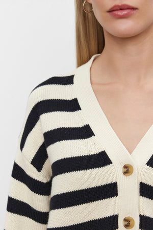 Close-up of a person wearing the ELODIE CARDIGAN by Velvet by Graham & Spencer, featuring a black and white striped pattern made from a cotton cashmere blend, three visible beige buttons, and a light-colored collar. One gold hoop earring is partially visible, set against a plain white background.