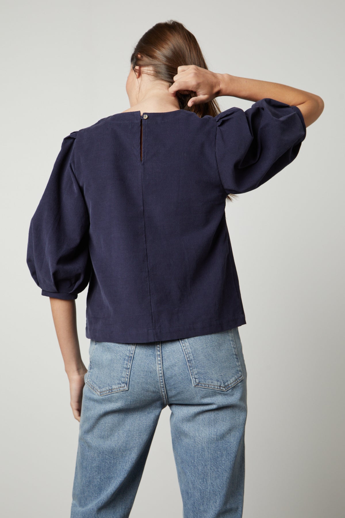   The back view of a woman wearing TARAH CORDUROY TOP by Velvet by Graham & Spencer jeans and a blue puff sleeve top. 