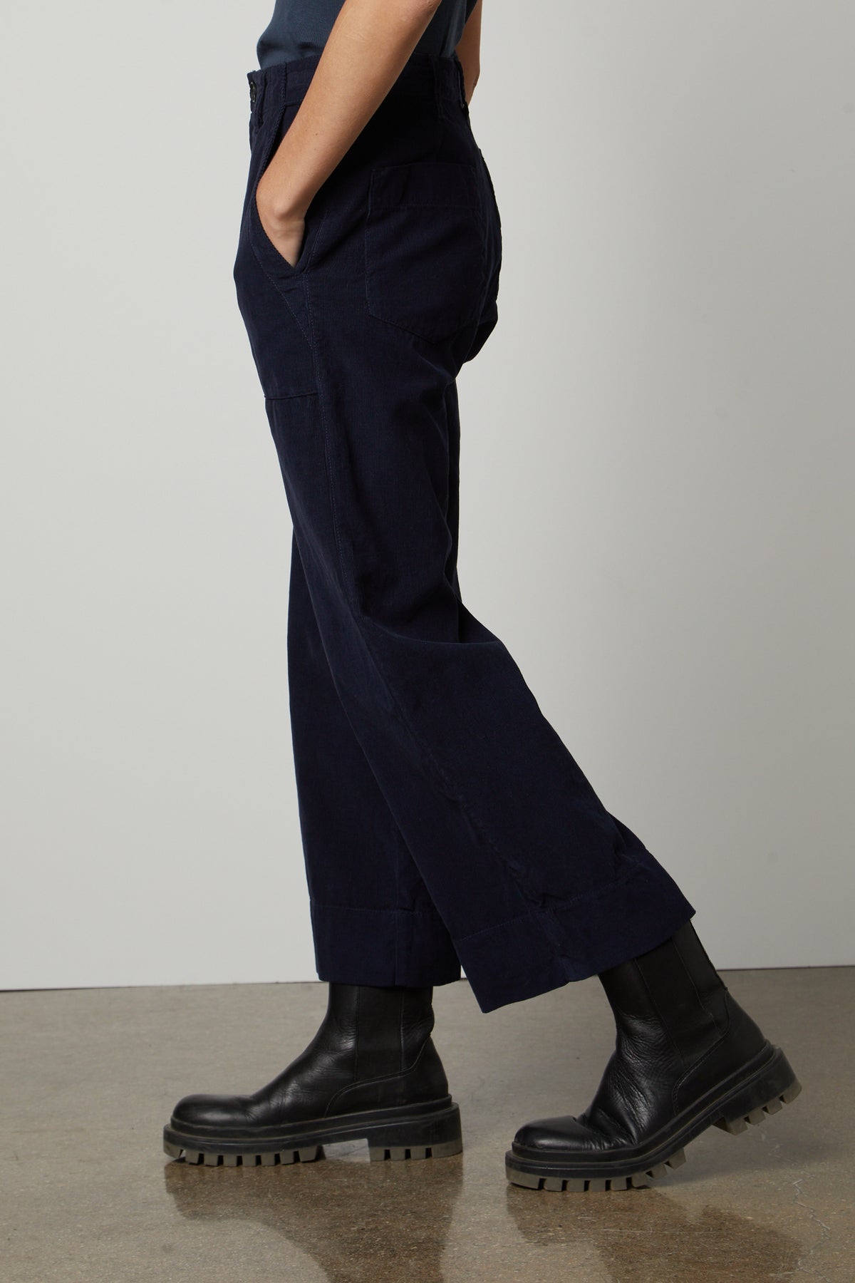 A woman in a blue shirt and black boots is standing in front of a white wall wearing the Velvet by Graham & Spencer VERA CORDUROY WIDE LEG PANT.-26727714193601