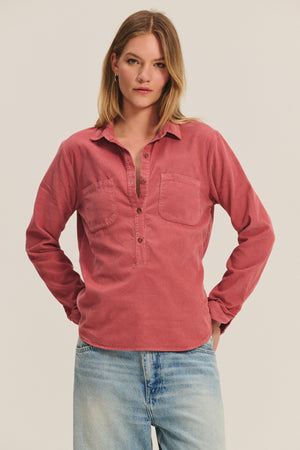 A person wears the ARIELLE CORDUROY SHIRT by Velvet by Graham & Spencer—a long-sleeve, dusty pink style with two chest pockets—paired with light blue jeans against a plain background. A must-have for any fall wardrobe.