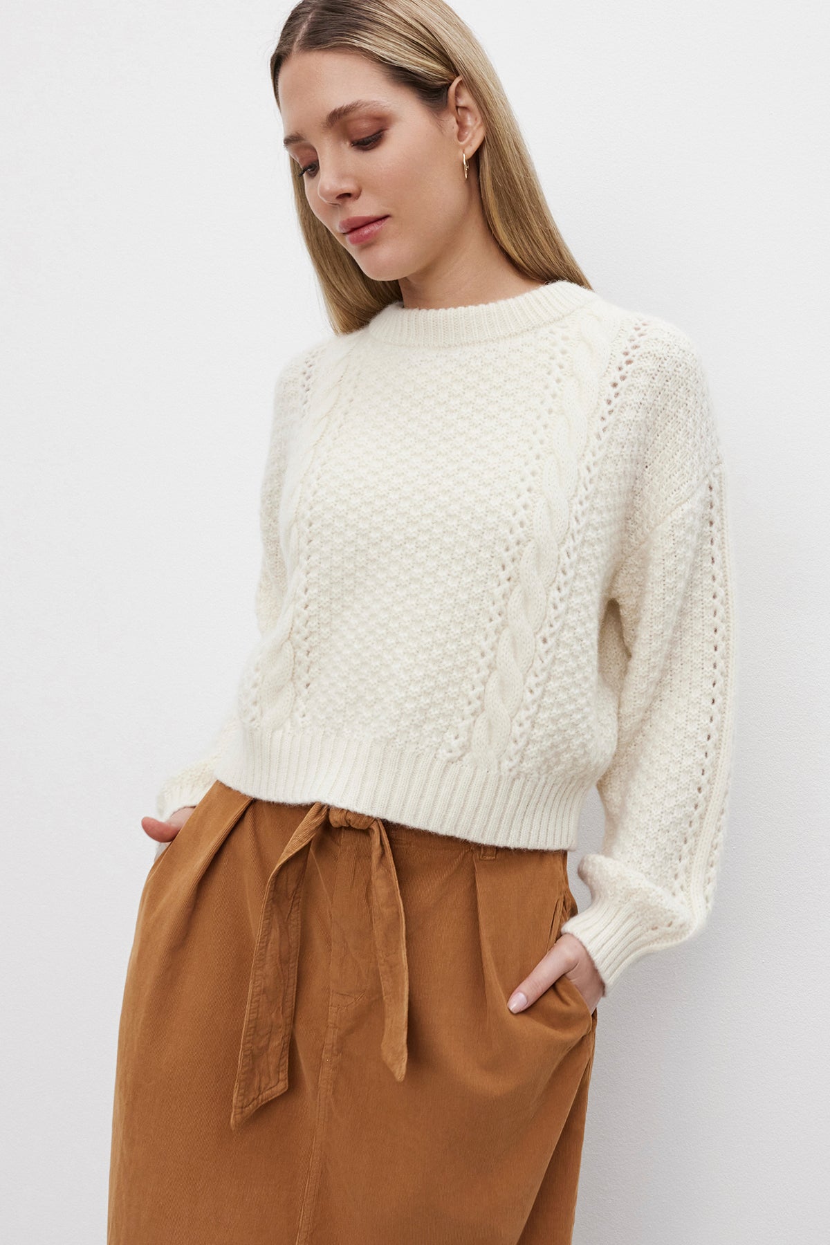   A woman with long blonde hair wears the MARLEY SWEATER, an alpaca blend cream knit sweater by Velvet by Graham & Spencer, along with brown high-waisted pants, standing against a plain white background. 