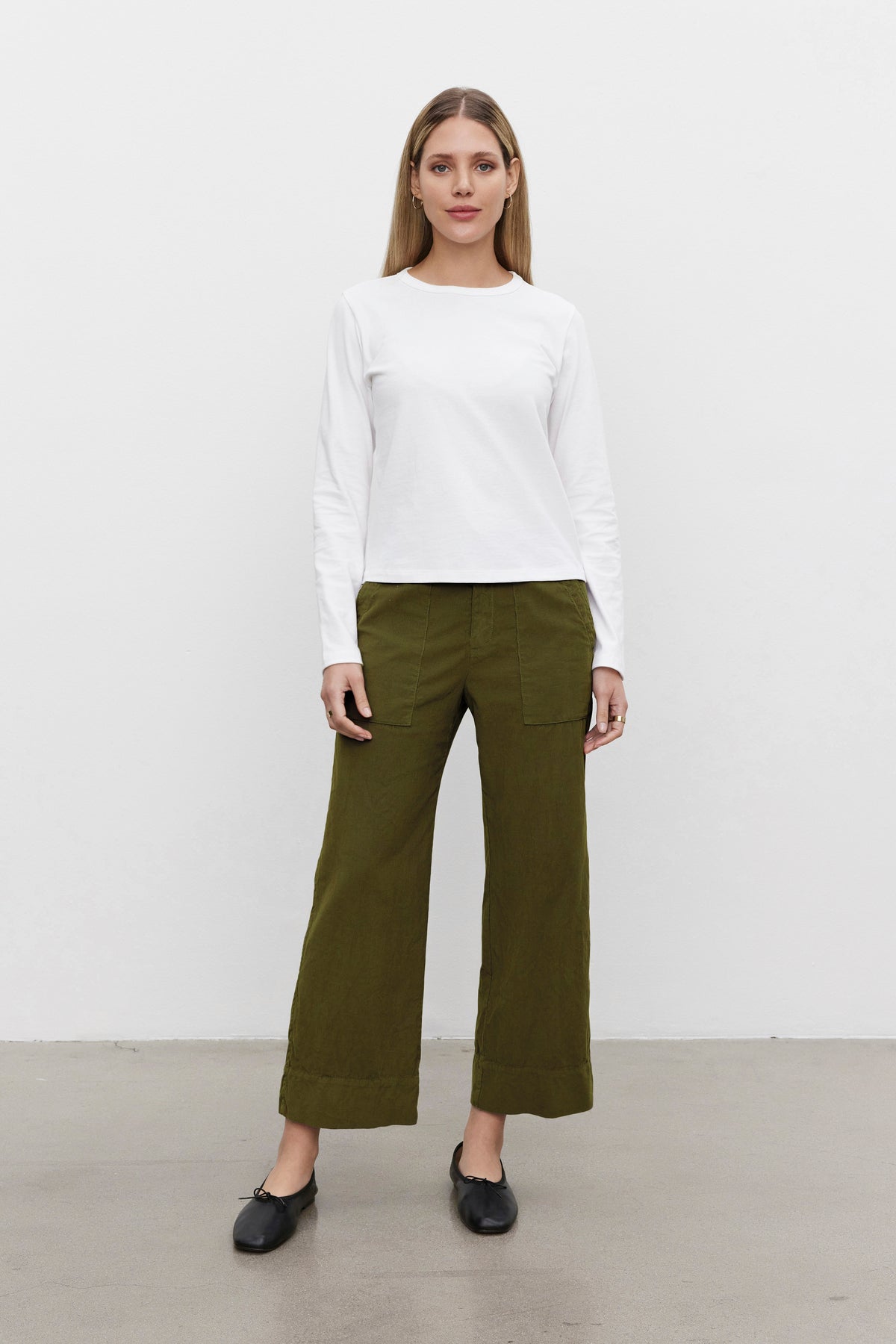   A person stands against a plain white background wearing a white long-sleeve shirt, the VERA CORDUROY PANT by Velvet by Graham & Spencer in olive green, and black shoes. 