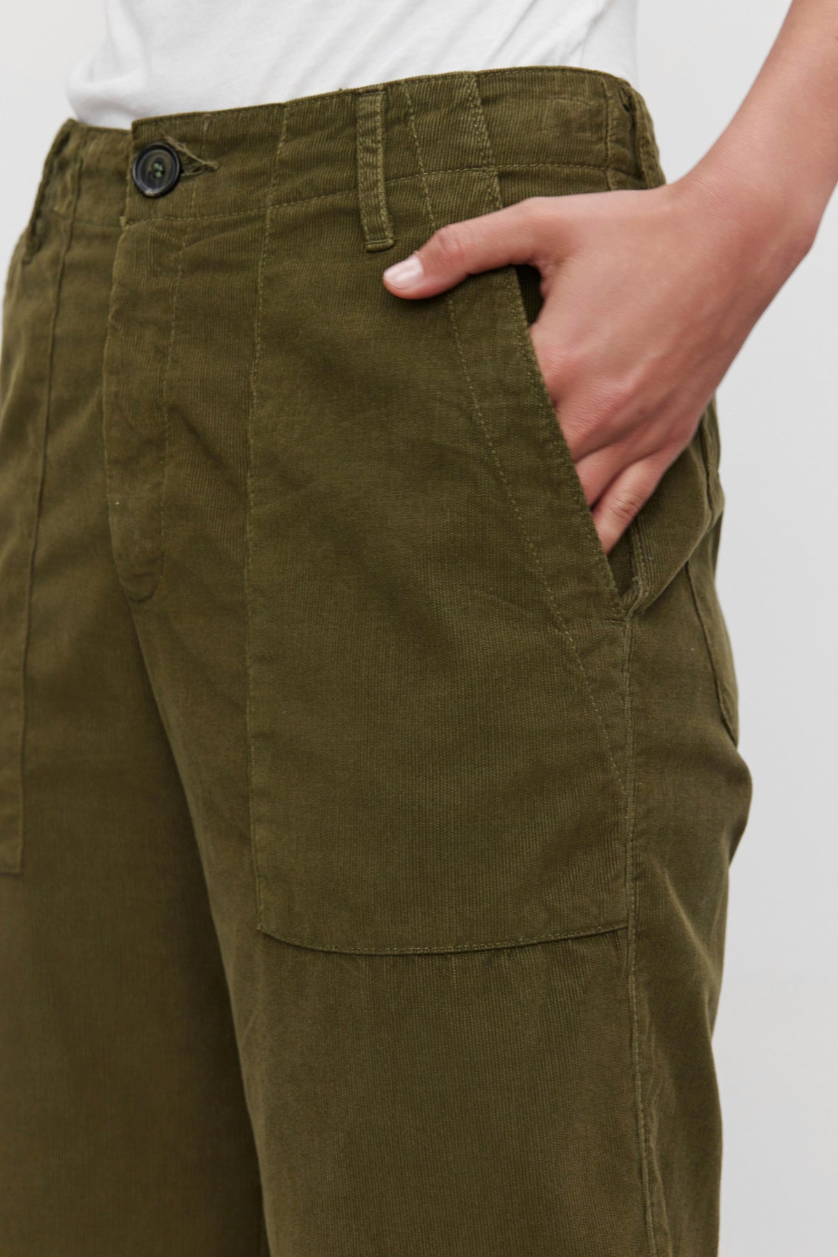   Close-up of a person wearing the VERA CORDUROY PANT from Velvet by Graham & Spencer in green, featuring pinwale corduroy fabric and cropped wide legs, with one hand in the pocket and a white shirt partially visible at the top. 