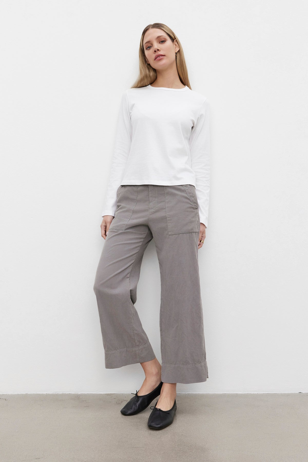   Person standing against a white background, wearing the SUSANNA TEE from Velvet by Graham & Spencer, paired with gray wide-leg pants and black flat shoes. The shirt features a classic crew neckline and is made from mid-weight cotton jersey fabric that enhances its vintage-inspired look. 