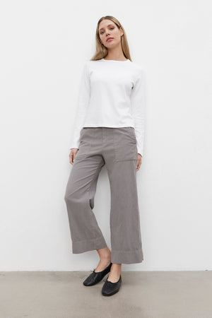 Person standing against a white background, wearing the SUSANNA TEE from Velvet by Graham & Spencer, paired with gray wide-leg pants and black flat shoes. The shirt features a classic crew neckline and is made from mid-weight cotton jersey fabric that enhances its vintage-inspired look.