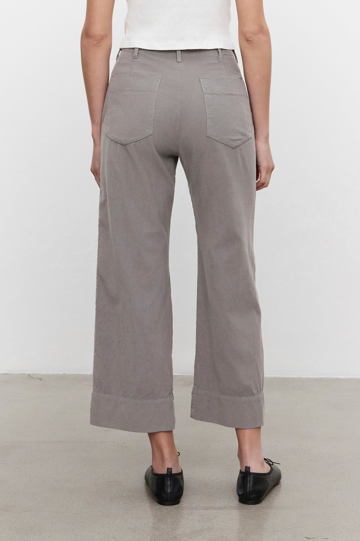 A person stands with their back to the camera, donning the VERA CORDUROY PANT in light gray by Velvet by Graham & Spencer, which creates a flattering silhouette. They pair it with black shoes against a plain background.-37676942491841