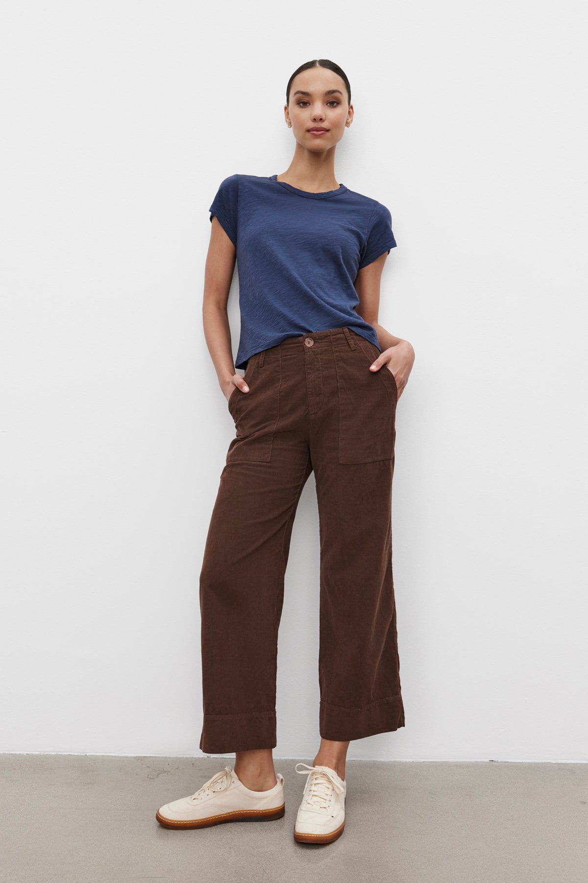   A person stands against a plain background wearing the MARIE TEE by Velvet by Graham & Spencer, a blue cotton slub t-shirt with a relaxed boxy fit, paired with brown wide-leg pants and hands in pockets, and white sneakers—perfect for a casual occasion. 