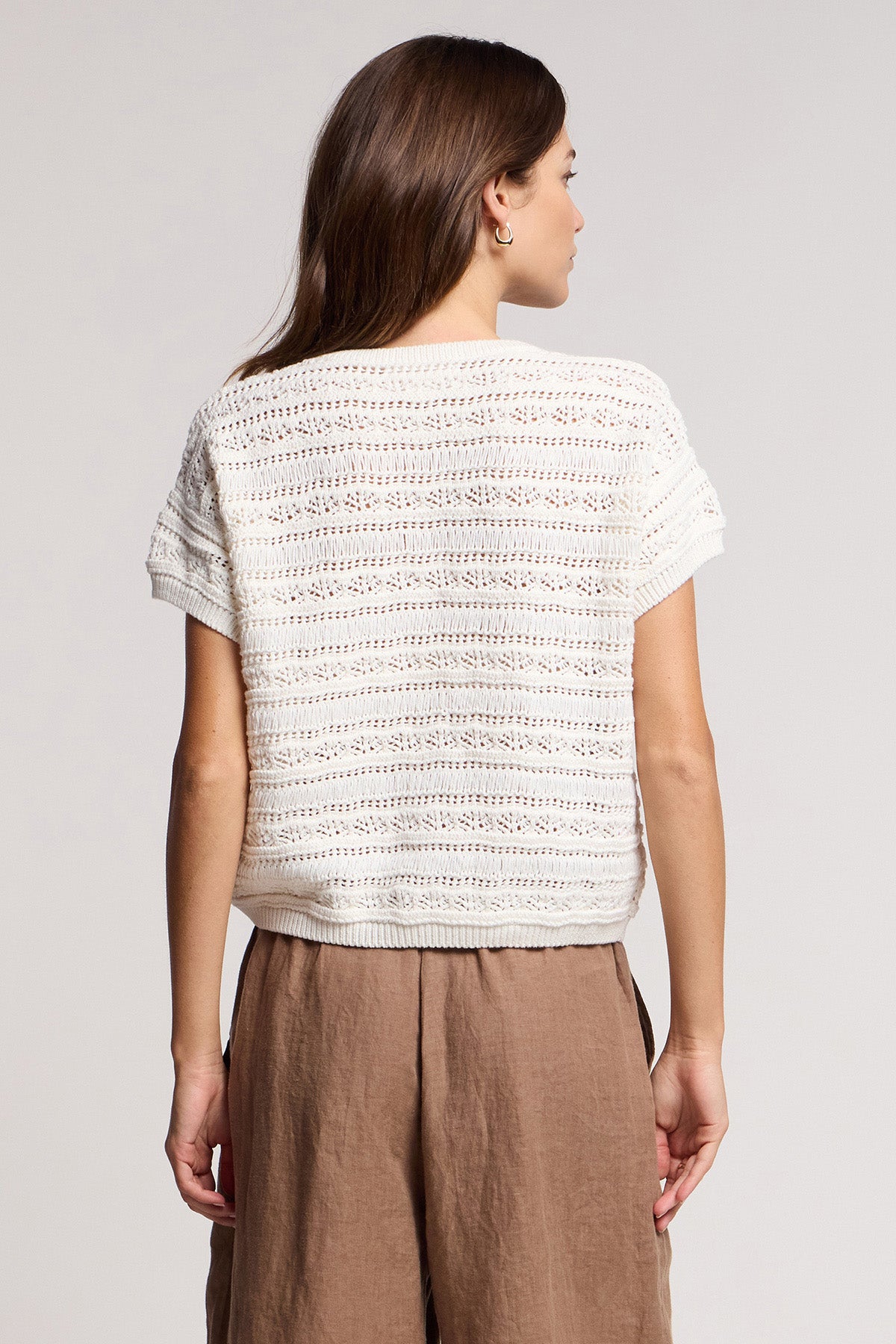 A woman faces away from the camera, wearing the BLOSSOM SWEATER in white by Velvet by Graham & Spencer and light brown high-waisted pants, set against a neutral background.-41644993118401