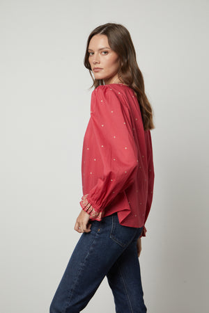 The model is wearing a red ANIA EMBROIDERED BOHO TOP by Velvet by Graham & Spencer, giving off a boho vibe.