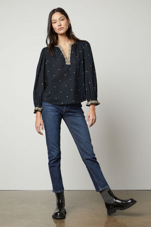 The model is wearing jeans and a black Velvet by Graham & Spencer ANIA EMBROIDERED BOHO TOP.