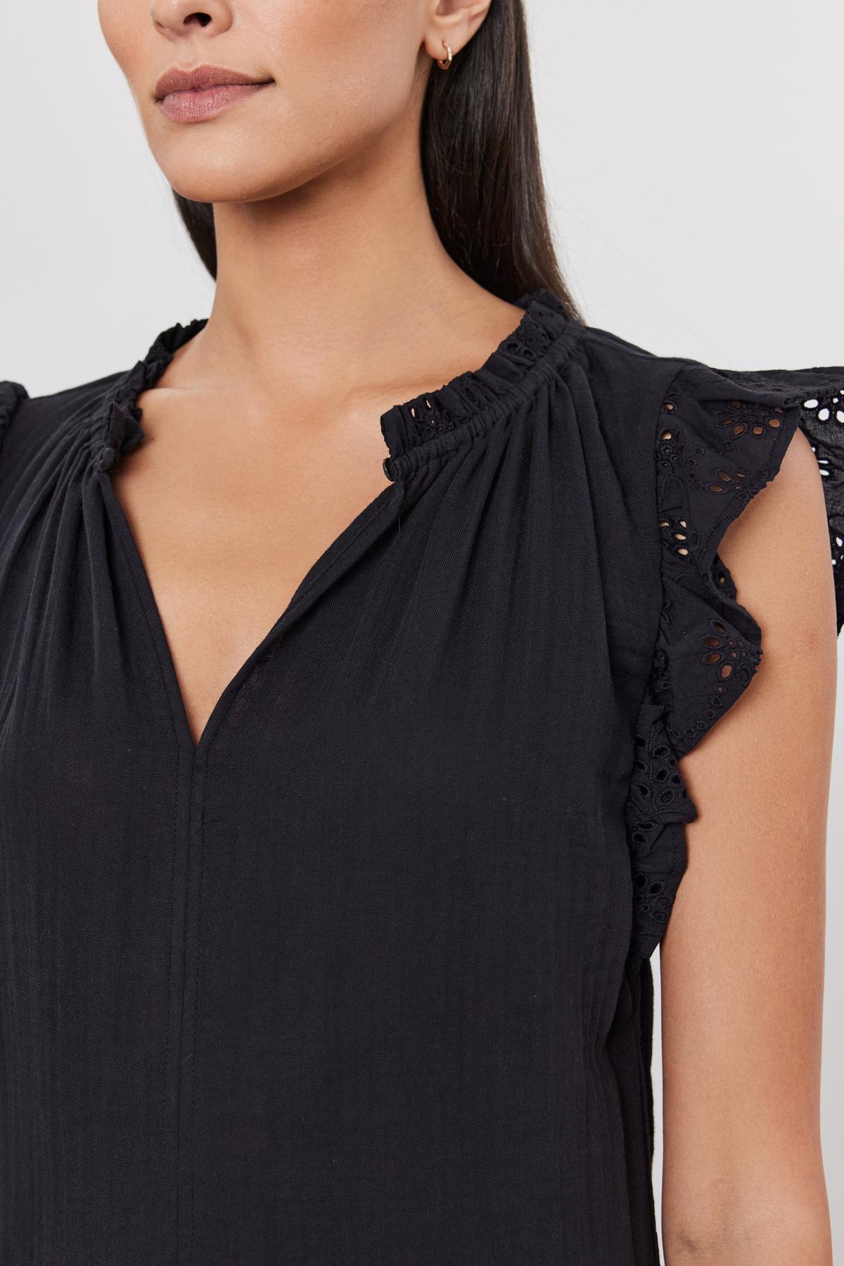   Close-up of a woman wearing a black blouse with cotton eyelet flutter sleeves and lace details by Velvet by Graham & Spencer's Grace Dress. 