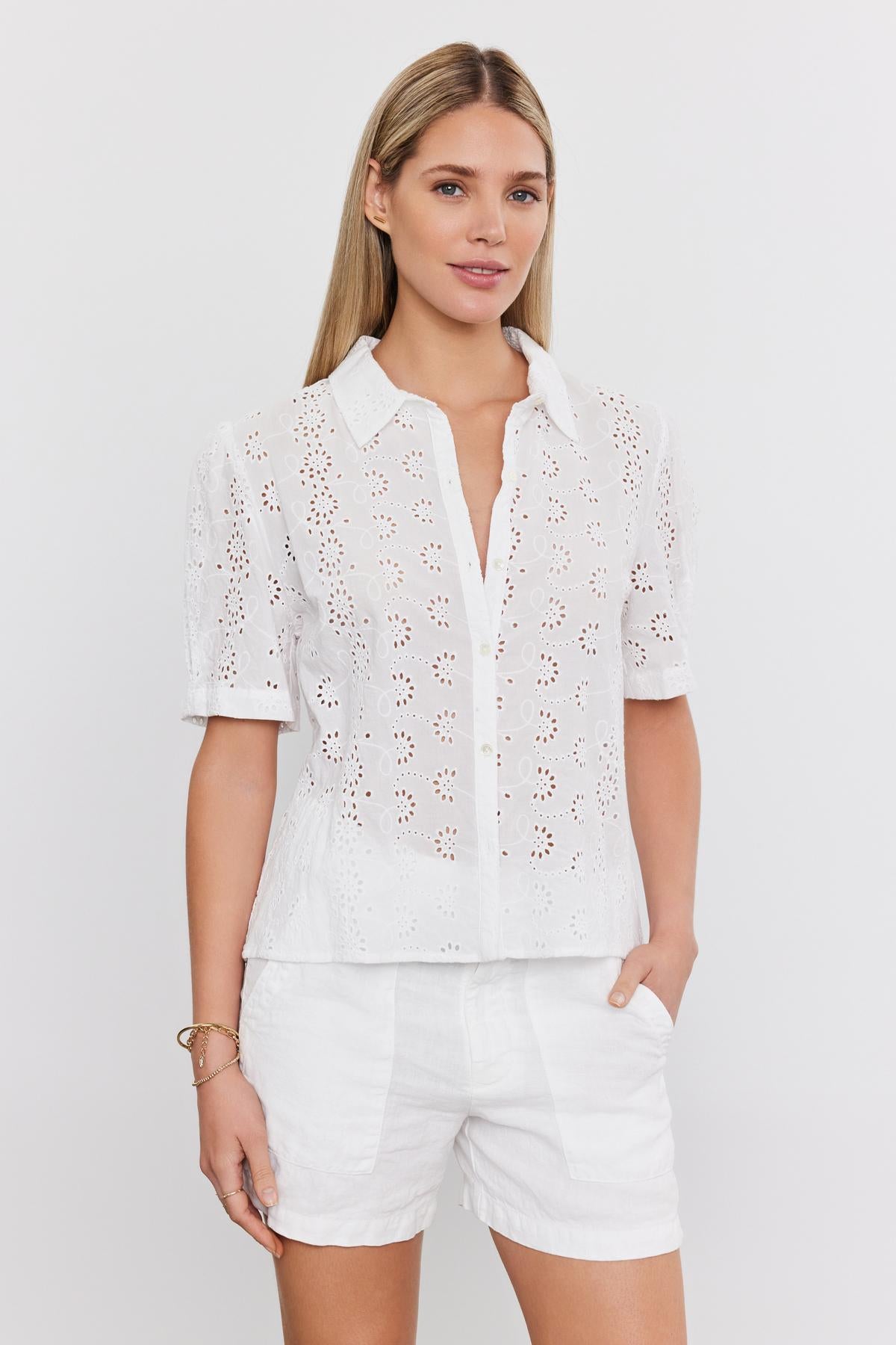   Woman wearing a white cotton OLIVIA BLOUSE with eyelet details and matching shorts standing against a plain background. (Velvet by Graham & Spencer) 