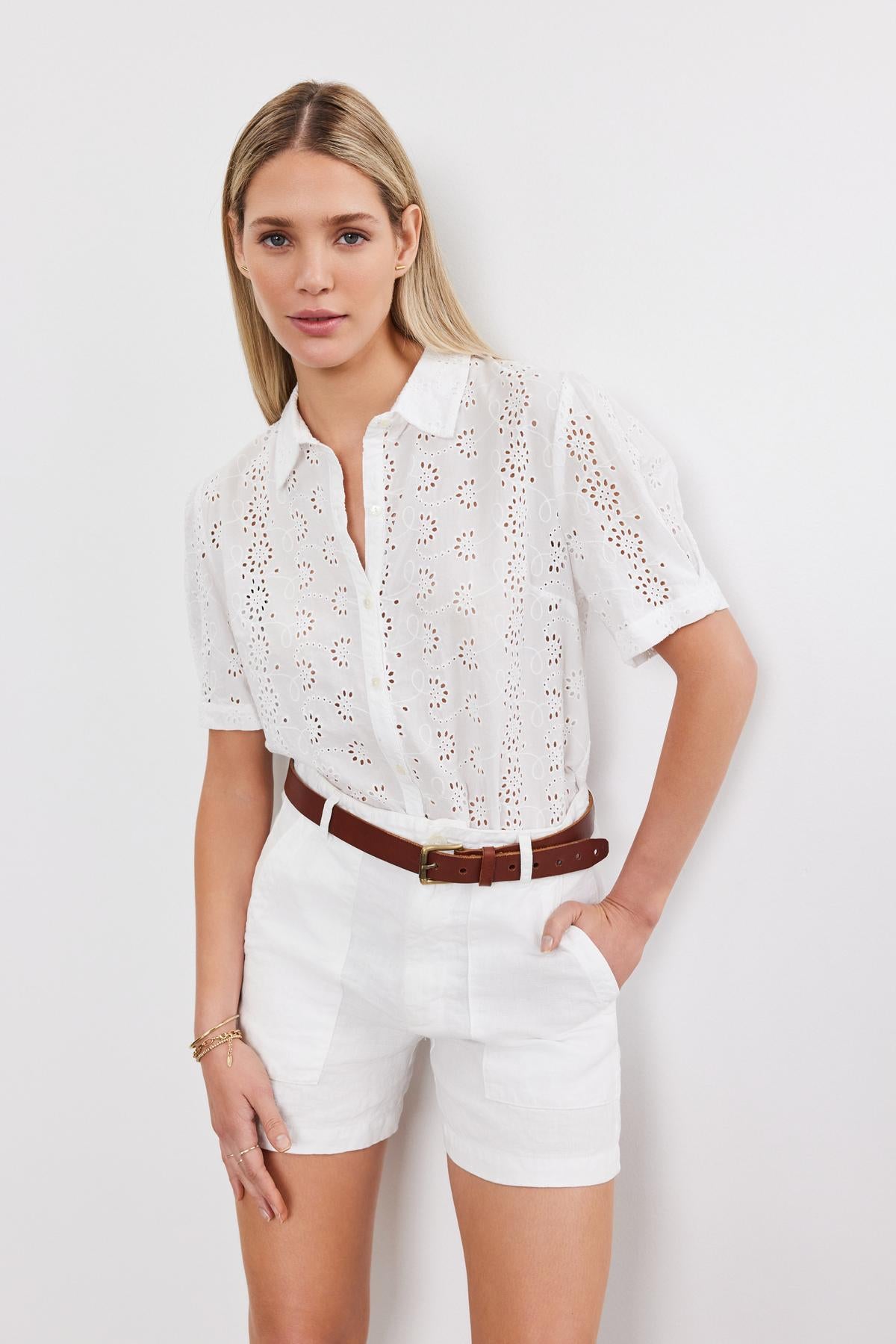 Young woman in a white cotton Olivia blouse with eyelet details and matching shorts with a brown belt, posing against a plain background. (Brand name: Velvet by Graham & Spencer)-36918784819393
