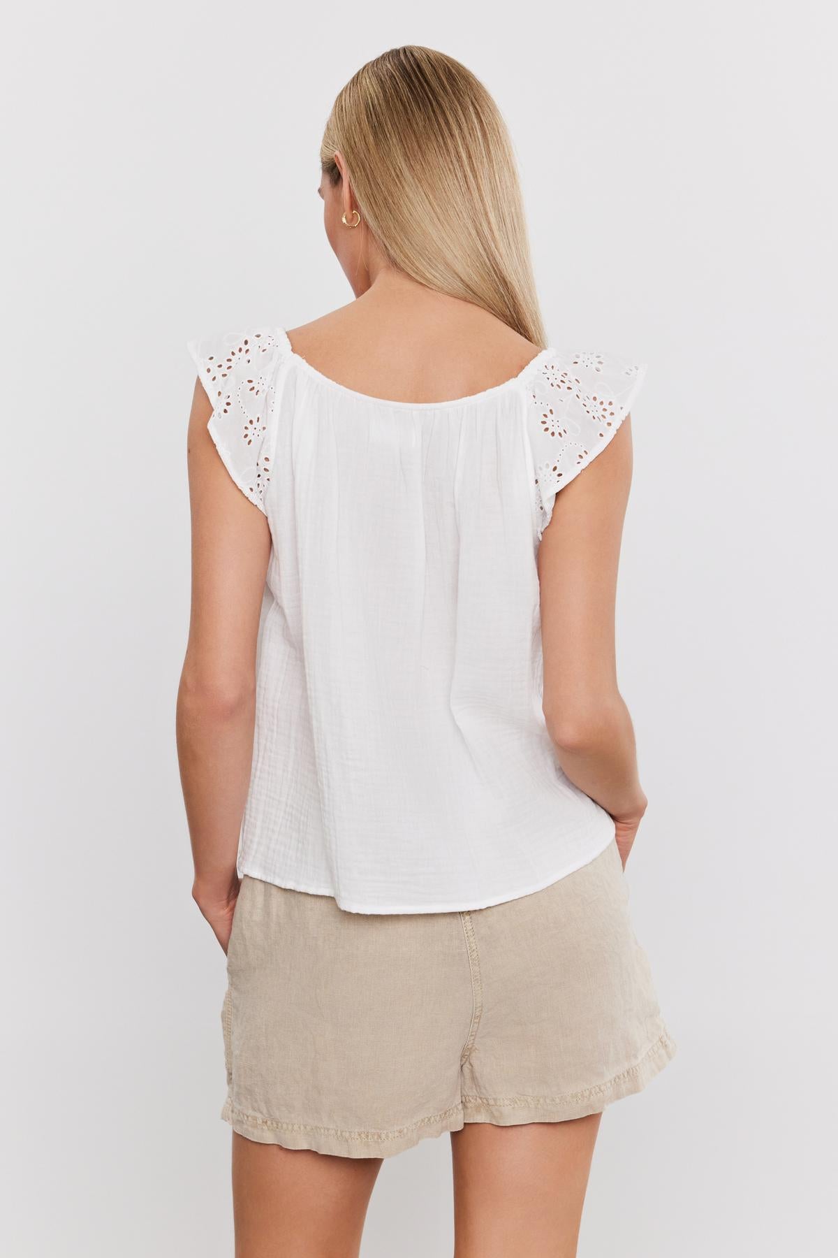   A person with long blonde hair is seen from behind wearing a STELLA TANK TOP by Velvet by Graham & Spencer and beige shorts. 