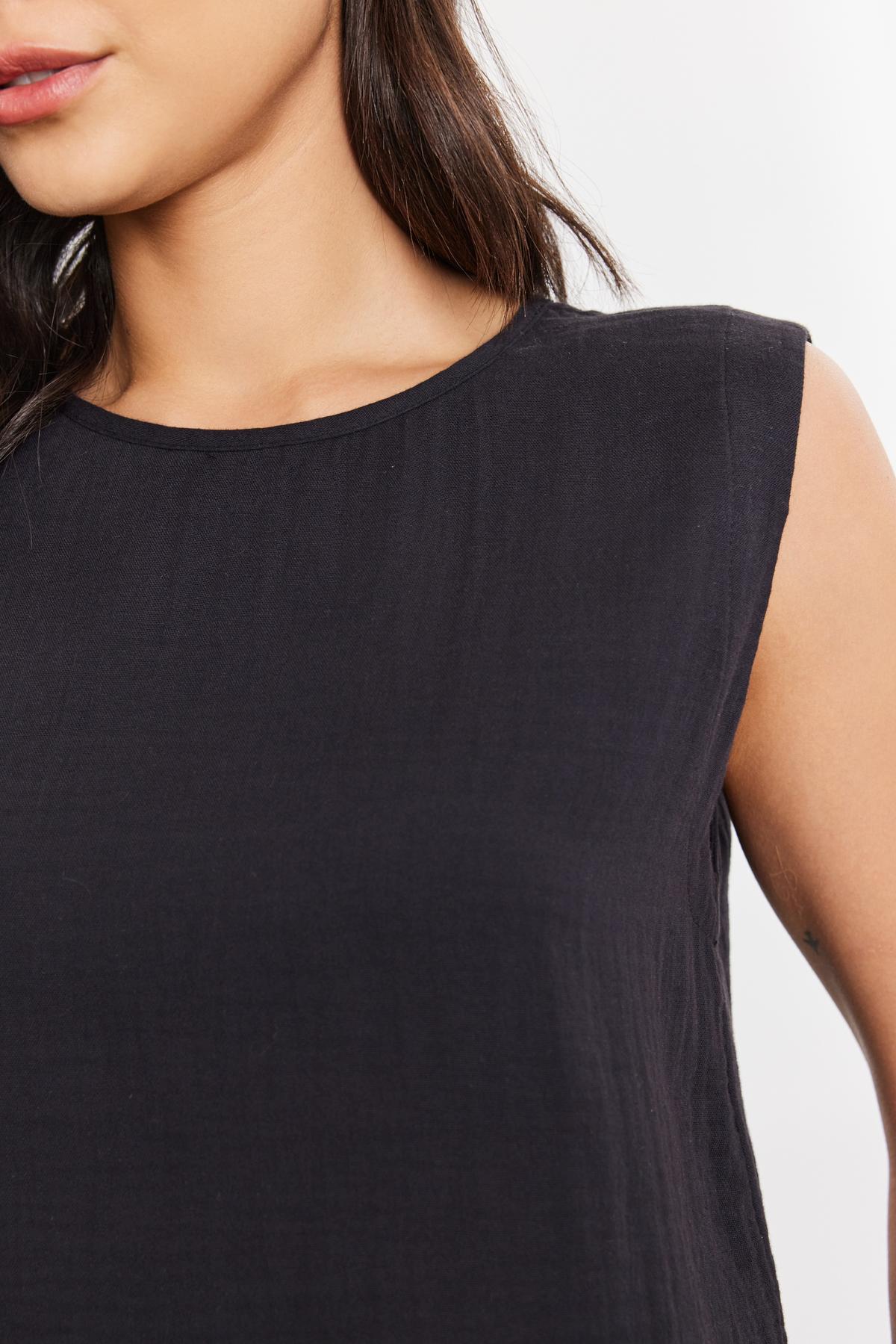   Close-up of a woman wearing a black Velvet by Graham & Spencer Aubren Cotton Gauze Tank Top, focusing on the shoulder and neckline area. Detail of fabric texture is visible. 