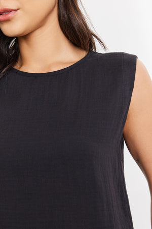 Close-up of a woman wearing a black Velvet by Graham & Spencer Aubren Cotton Gauze Tank Top, focusing on the shoulder and neckline area. Detail of fabric texture is visible.