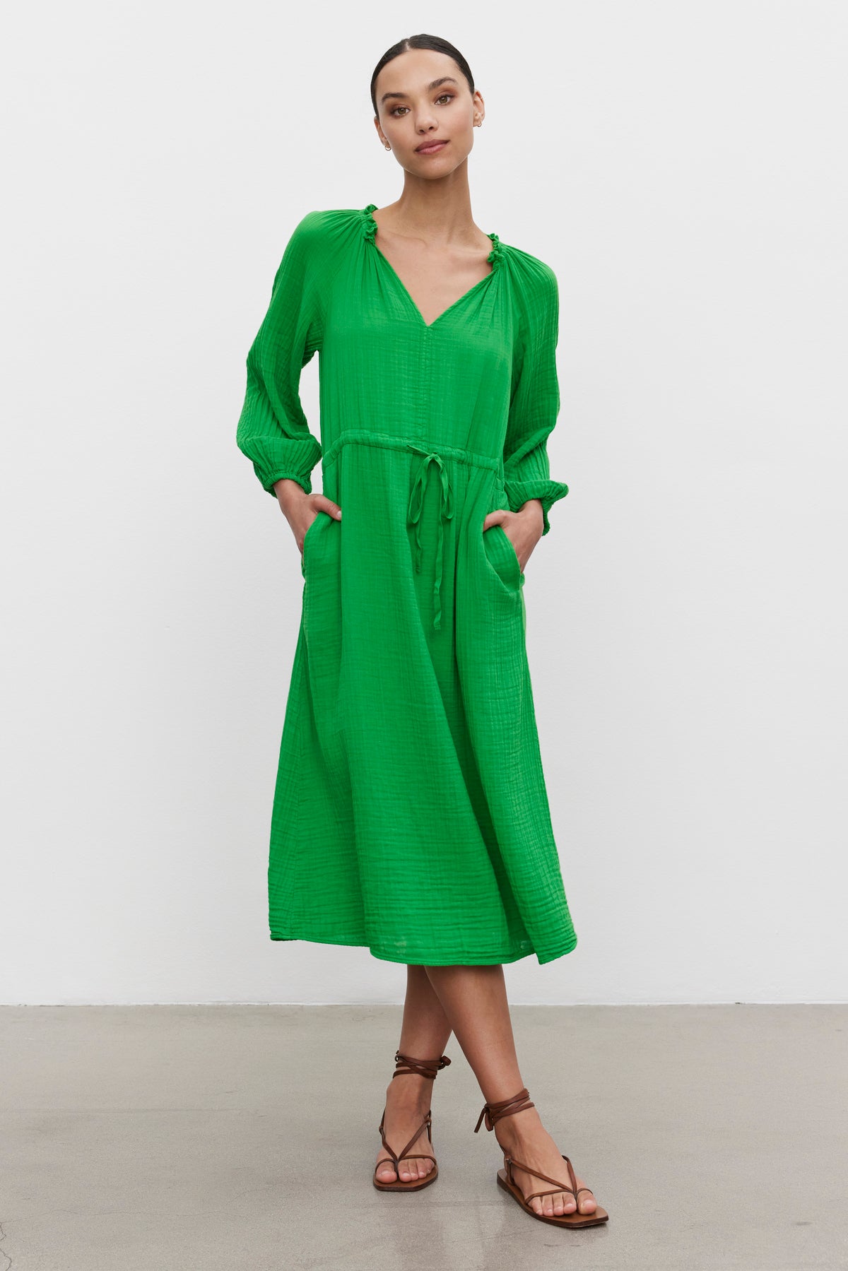 A woman models a green mid-length warm weather AUDREY COTTON GAUZE DRESS by Velvet by Graham & Spencer with gathered details and brown strappy sandals, accessorized perfectly for vacation.-36247882367169