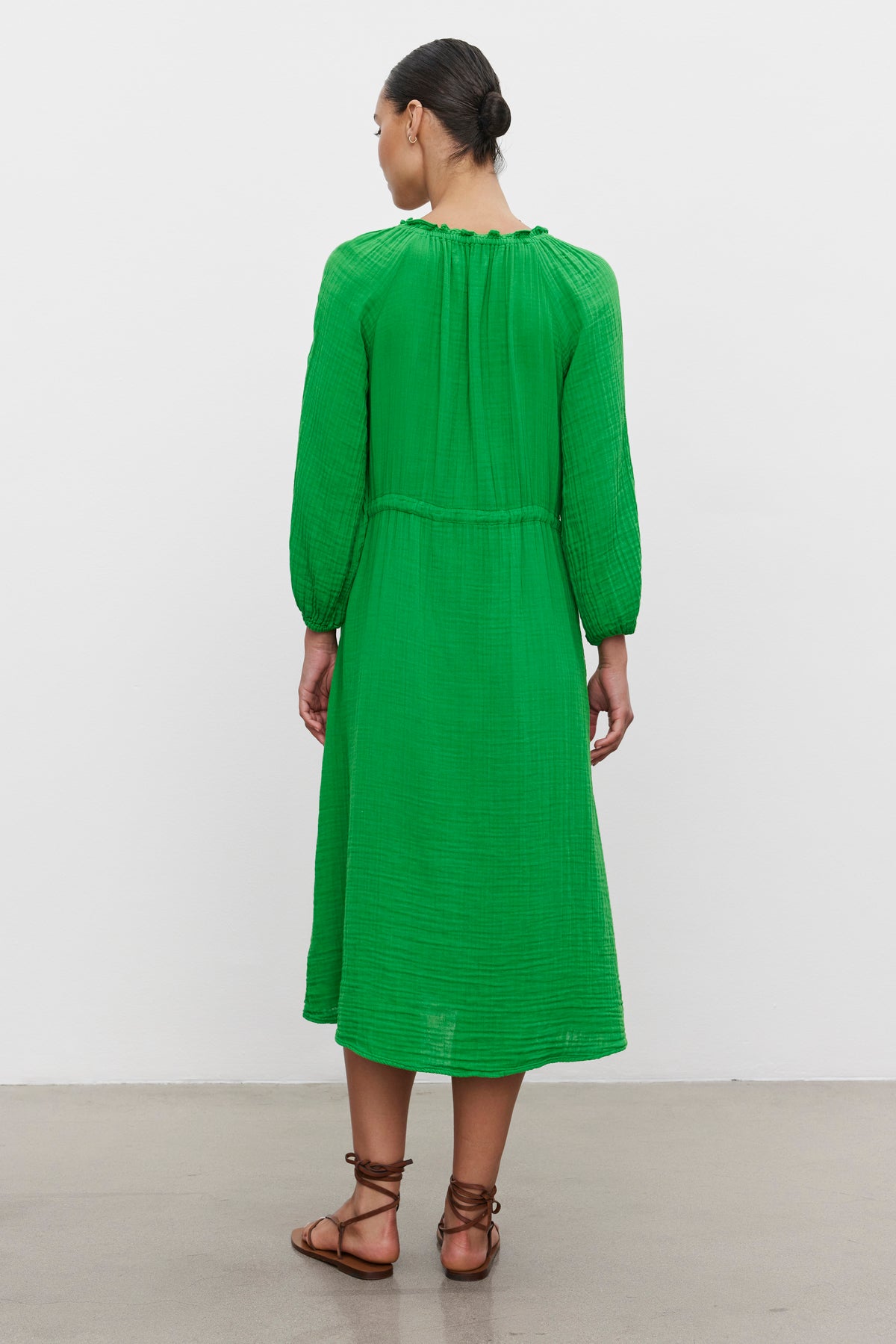   Woman standing with her back to the camera, wearing a green mid-length warm weather AUDREY COTTON GAUZE DRESS with gathered detailing, accessorized with brown sandals by Velvet by Graham & Spencer. 