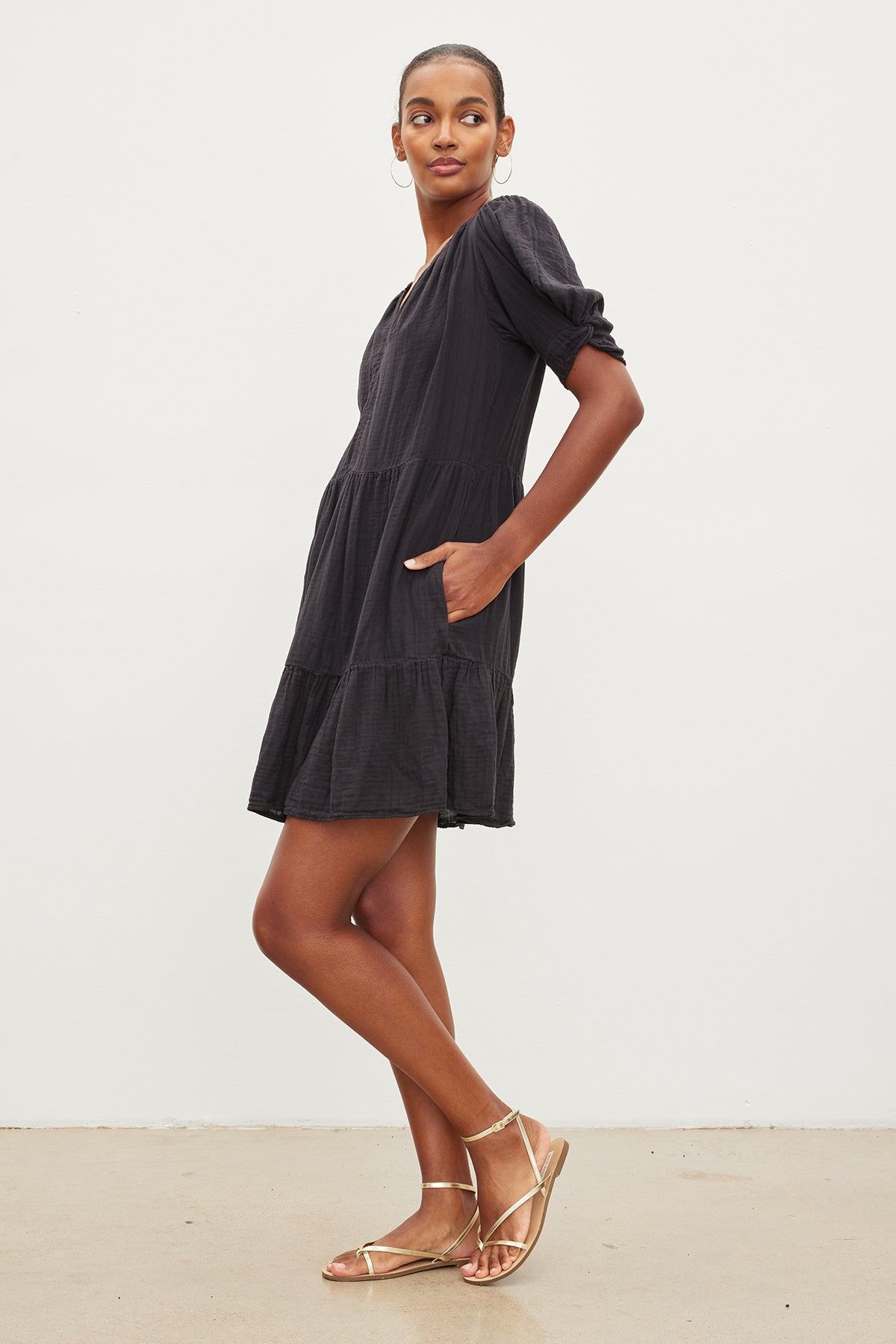   The model is wearing a Velvet by Graham & Spencer black BELLA COTTON GAUZE DRESS with a ruffle sleeve and sandals. 