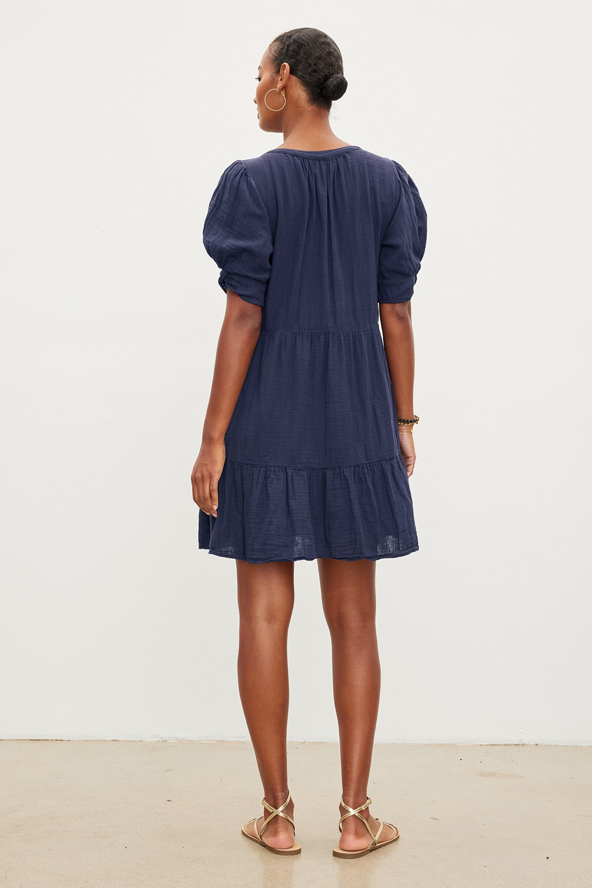   A person with short hair wearing a navy blue BELLA COTTON GAUZE DRESS by Velvet by Graham & Spencer and sandals is standing with their back to the camera against a plain white background. 