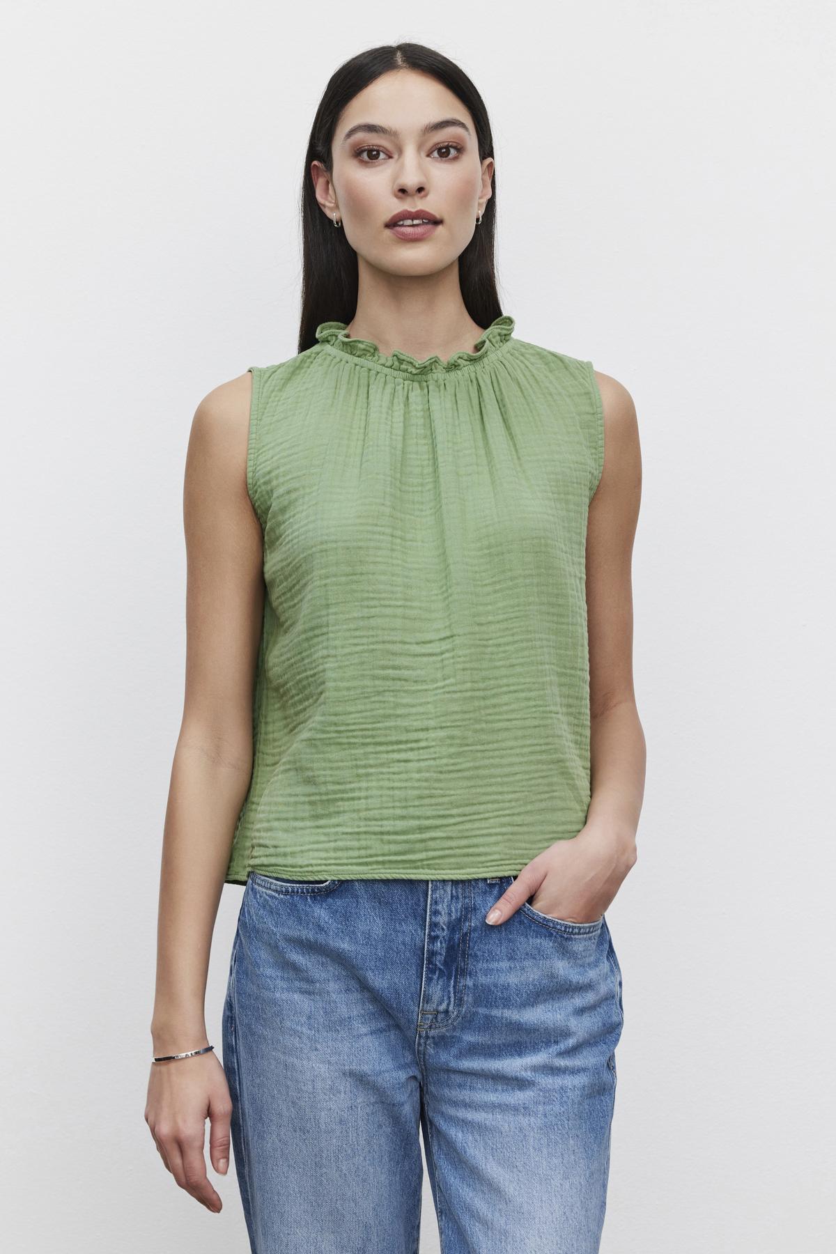   A person with long dark hair is wearing a green BIANCA COTTON GAUZE TANK TOP by Velvet by Graham & Spencer and blue jeans, standing against a plain white background. 