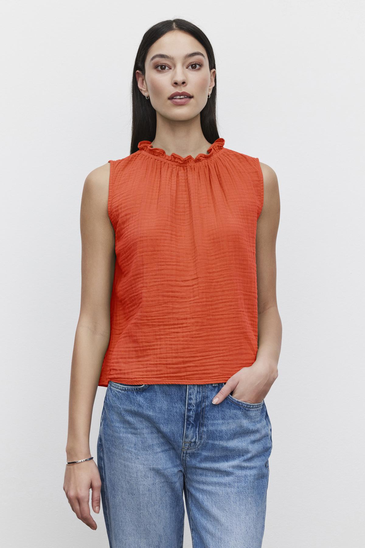   A person with long dark hair is wearing a sleeveless red BIANCA COTTON GAUZE TANK TOP by Velvet by Graham & Spencer and light blue jeans, standing against a plain white background. 