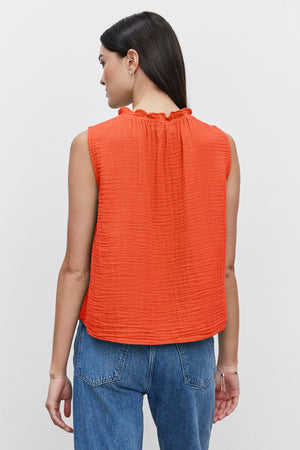 A woman with long straight hair is wearing a sleeveless orange BIANCA COTTON GAUZE TANK TOP by Velvet by Graham & Spencer and blue jeans. She is facing away from the camera, showing the back of her outfit.