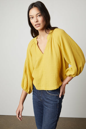 The model is wearing a yellow CARLA COTTON GAUZE TOP with sleeve ruffles by Velvet by Graham & Spencer.
