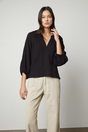 The model is wearing a relaxed-fit Velvet by Graham & Spencer Carla Cotton Gauze Top and beige pants.