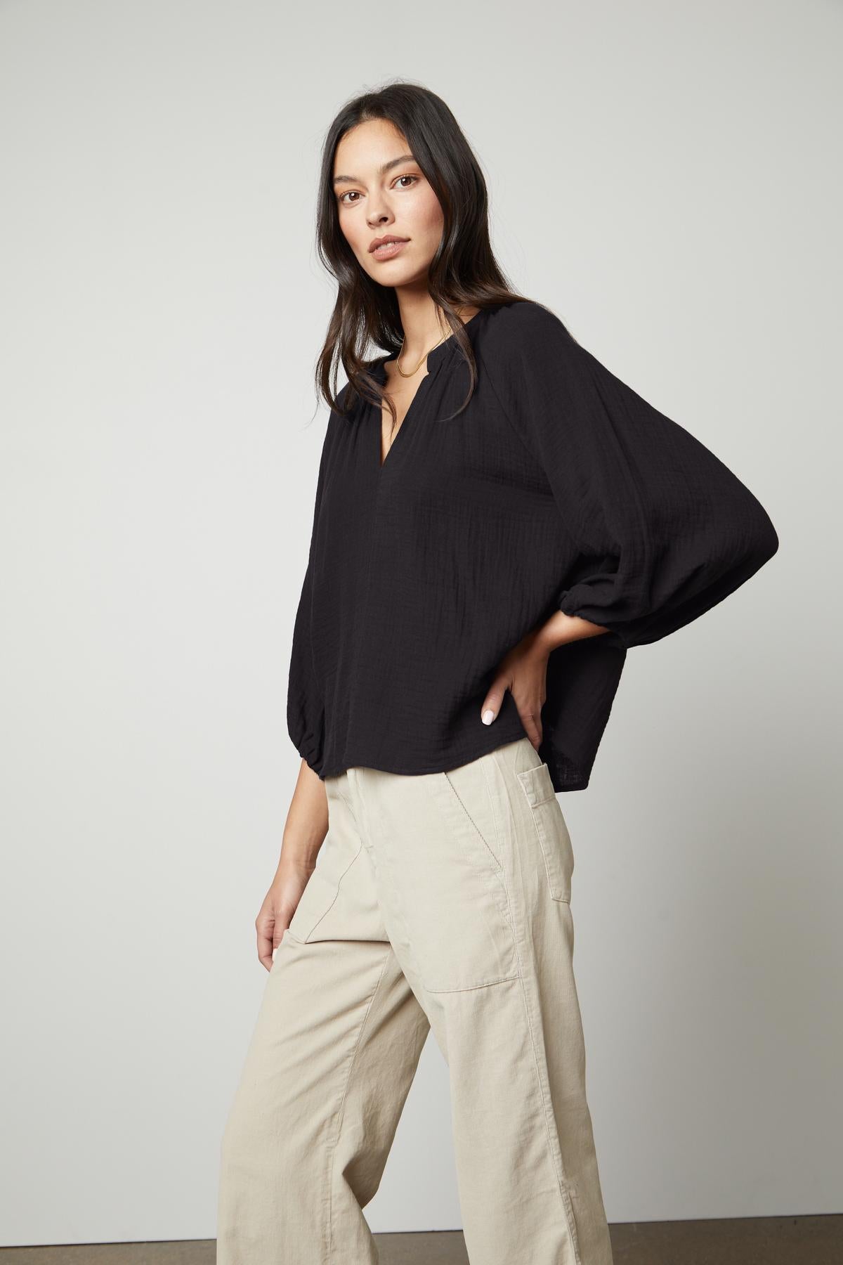   The model is wearing a relaxed-fit, black Velvet by Graham & Spencer top with a v-neckline and beige wide leg pants. 