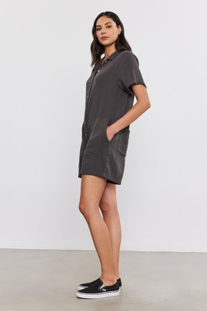 A woman in a gray short-sleeve Dane Cotton Gauze Romper by Velvet by Graham & Spencer and black sneakers standing in a studio setting.